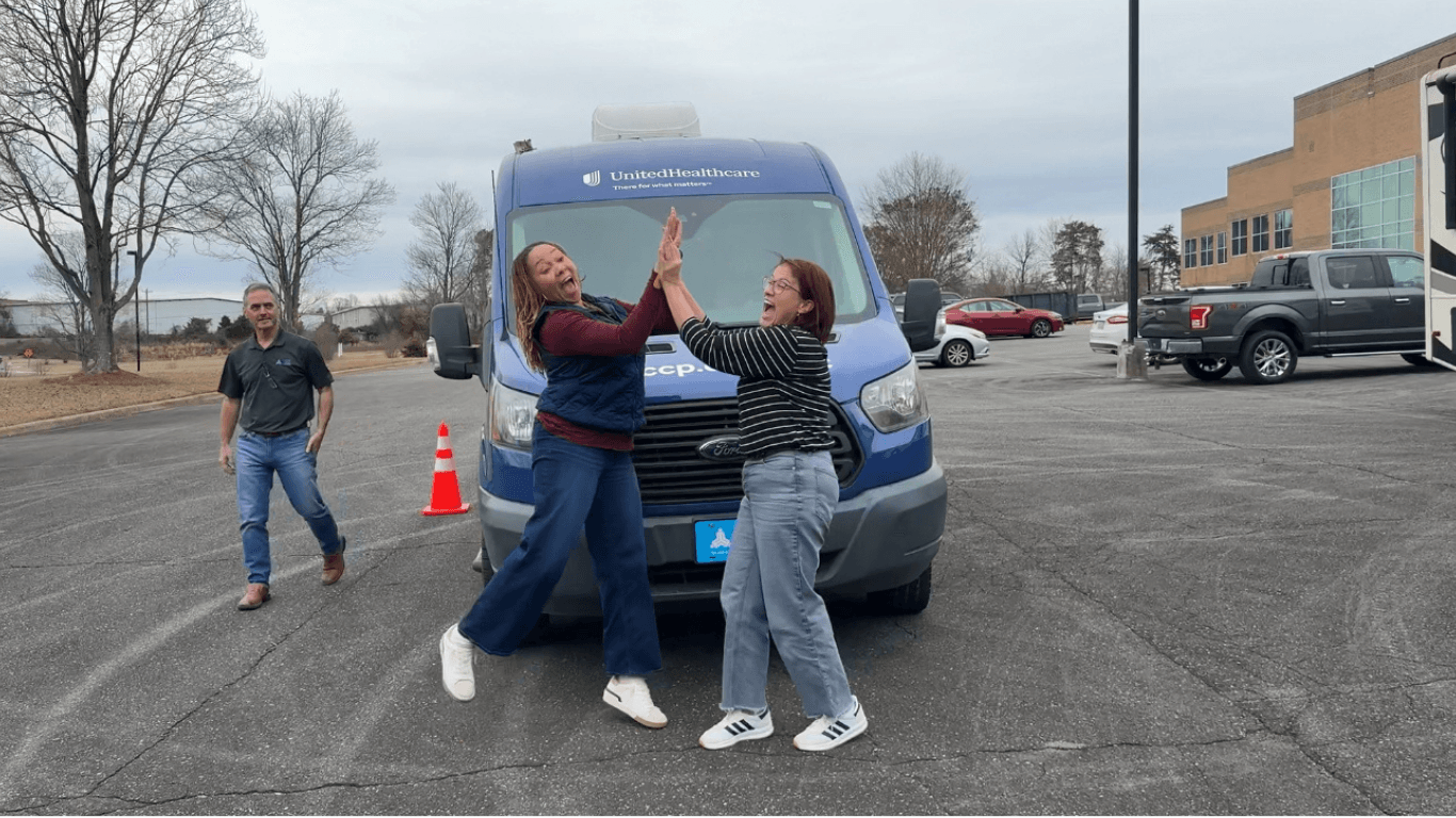 Two operators high-fiving in front of a UnitedHealthcare mobile clinic after completing operator training